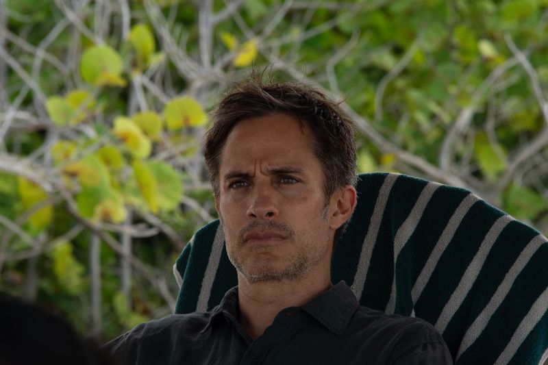 Primer plano del actor Gael García Bernal con expresión seria y pensativa sentado en una silla reclinable en un entorno natural.