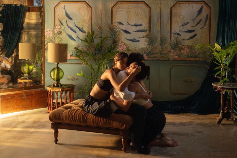 Fotograma dramático de tres personajes abrazados en el suelo de una habitación elegante con decoración tropical.