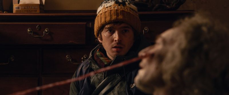 Bryan observando una mutación en Resident Evil: Noche Cero Primer plano de Bryan con un gorro tejido mirando fijamente con expresión atónita y desconcertada hacia una criatura u organismo con tentáculos que se extiende frente a él.