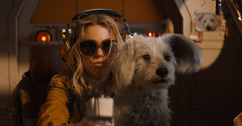 Fotograma de la película dentro de la cabina de una nave espacial donde Kara (Milly Alcock) aparece usando gafas de sol retro y audífonos de piloto junto a Krypto el Superperro mirando hacia el frente. supergirl-kara-zor-el-krypto-nave-espacial.jpg