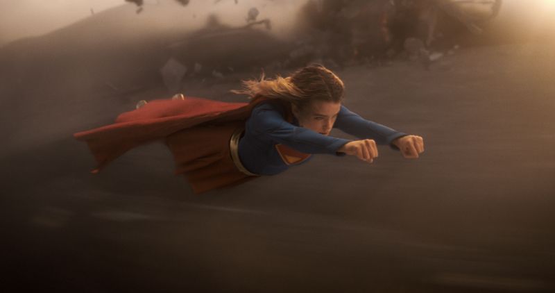 Supergirl en pleno vuelo Secuencia de acción que muestra a Supergirl volando a gran velocidad a baja altura a través de un entorno desértico envuelto en polvo y viento.