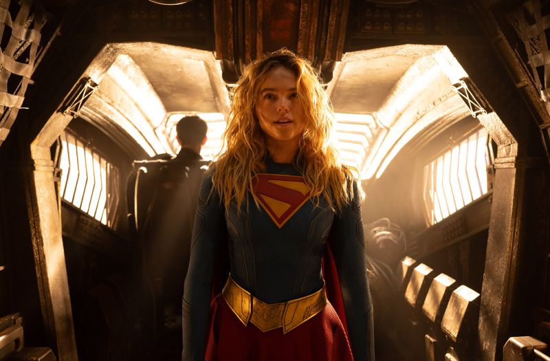 Supergirl en el pasillo de la nave Plano frontal de Kara Zor-El con el traje de Supergirl en el pasillo de una nave espacial iluminado por una cálida luz dorada de fondo.