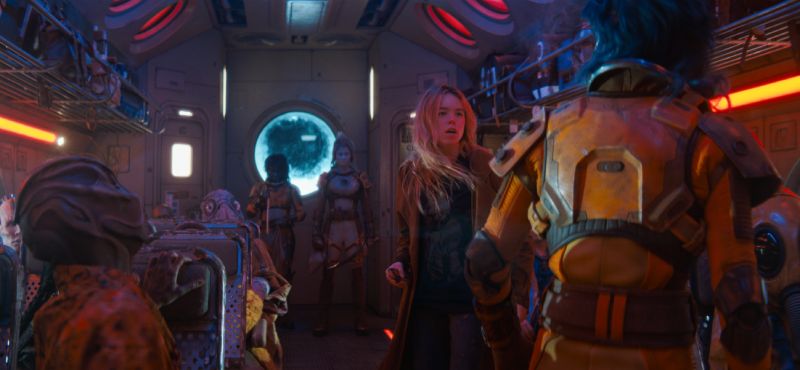 Viaje galáctico en Supergirl Fotograma del interior de un transporte espacial repleto de diversas criaturas e individuos alienígenas, con Kara en el centro reaccionando sorprendida.
