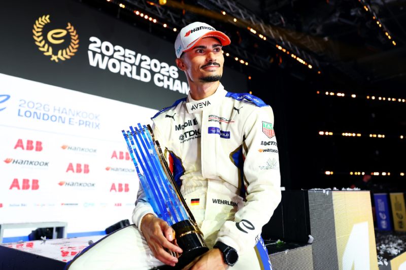 Fotografía del piloto Pascal Wehrlein vistiendo su uniforme de careras blanco y azul con gorra mientras sostiene el trofeo del campeonato mundial frente a un fondo del evento.