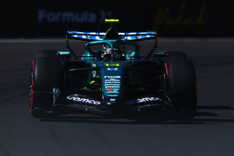 Fernando Alonso en el Gran Premio de España de F1 Fotografía frontal del monoplaza de Fórmula 1 de la escudería Aston Martin, conducido por el piloto español Fernando Alonso sobre el trazado del Gran Premio de España, destacando la toma aérea verde sobre el casco del conductor y la luz frontal sobre el asfalto.