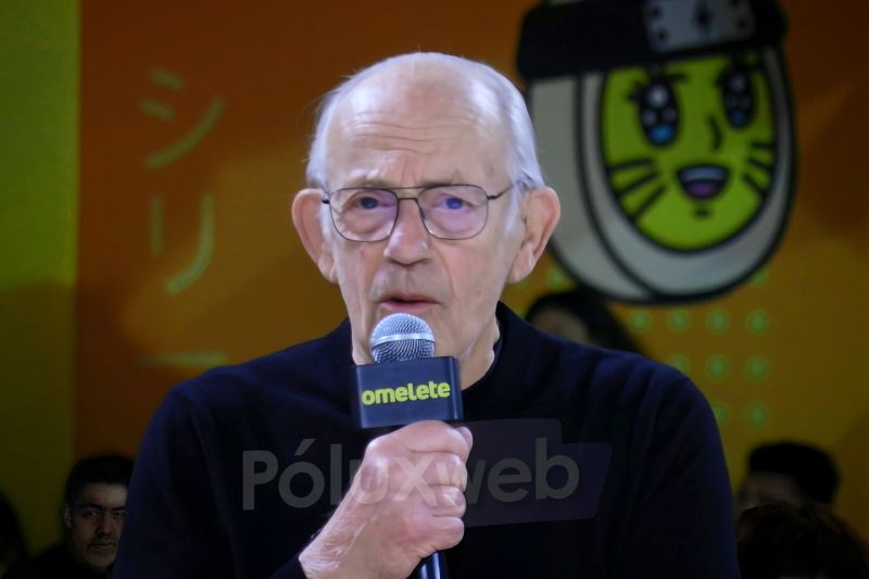 Persona mayor sosteniendo un micrófono en un escenario con fondo ilustrado y estética pop cultural.
