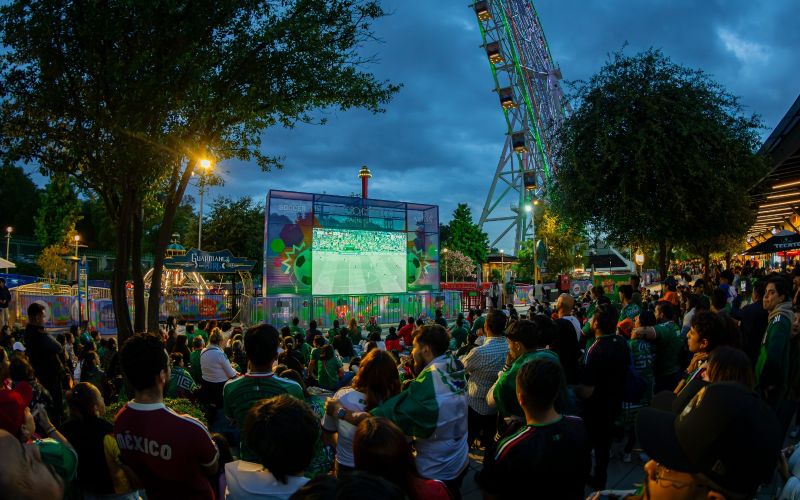 Multitud reunida en un espacio público observando un partido de futbol en pantalla gigante.