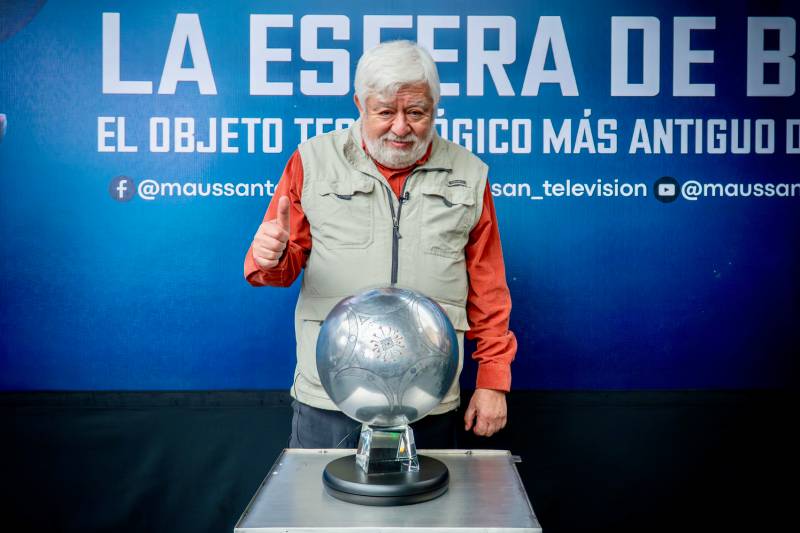 Fotografía de Jaime Maussan posando junto a una esfera metálica colocada sobre un pedestal, con un fondo azul que anuncia su presentación pública.