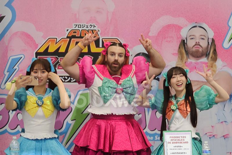 Presentación de Babybeard en AniMole 4 Integrantes del grupo Babybeard posando en el escenario frente a su lona promocional rosa; al centro, Ladybeard luciendo un traje rosa de magical girl con moños, flanqueado por las dos cantantes con trajes azules.