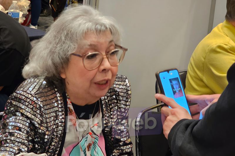 Rocío Garcel en el Doblaje Alley de AniMole 4 La actriz de doblaje Rocío Garcel con saco de lentejuelas brillantes conversando atentamente con un asistente mientras graba un saludo en un teléfono celular.