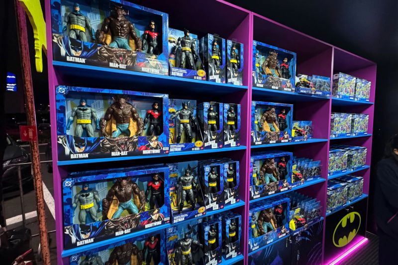 Zona de Coleccionables en Batman Day 2026 Estantes de exhibición de color morado cargados de figuras de acción y coleccionables de Batman, Man-Bat y Nightwing.