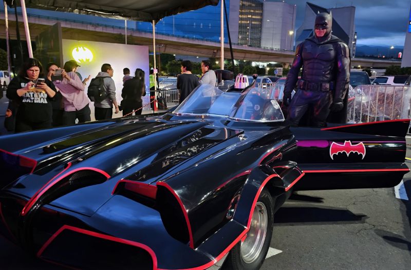 Batimóvil de 1966 en Batman Day 2026 Una réplica del Batimóvil de la serie de televisión de 1966 de Adam West con un cosplayer de Batman posando junto a la puerta del conductor.