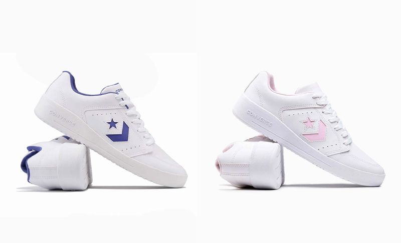 Calzado deportivo de la colección Converse Back to School 2026 Fotografía de producto con fondo blanco que muestra dos pares de tenis deportivos de corte bajo en color blanco; el par izquierdo presenta el logotipo en forma de estrella y chevrón junto con el forro interno en color morado, mientras que el par derecho lleva los mismos detalles en tono rosa pastel.
