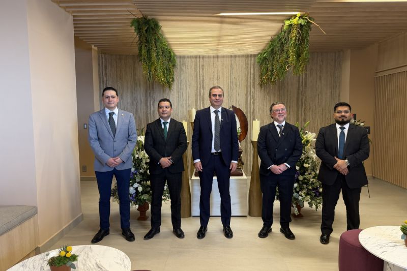 Cinco personas en traje posando en un espacio interior moderno con elementos naturales, arreglos florales y mobiliario contemporáneo.