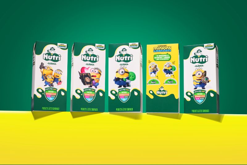 Colección de empaques de edición especial Nutri Banana y Minions & Monstruos Fotografía de estudio que exhibe cinco empaques en formato tetra pack de la edición especial Nutri Clásica en colaboración con la película Minions & Monstruos. Cuatro envases presentan fondo blanco con verde y personajes como Minions sosteniendo cámaras o portando disfraces, mientras que el envase central muestra un diseño amarillo interactivo con instrucciones para recortar y armar figuras. La composición descansa sobre una superficie amarilla y un fondo verde.