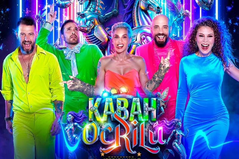 Cinco artistas posan con vestuarios neón en un entorno futurista lleno de luces y elementos fantásticos, evocando un espectáculo vibrante y visualmente explosivo.