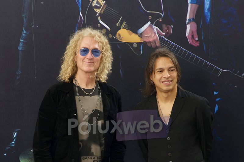 Bruce Watson con cabello rizado rubio y gafas de sol junto al vocalista Luis Carlos Maldonado sonriendo durante la conferencia de prensa de FOREIGNER.
