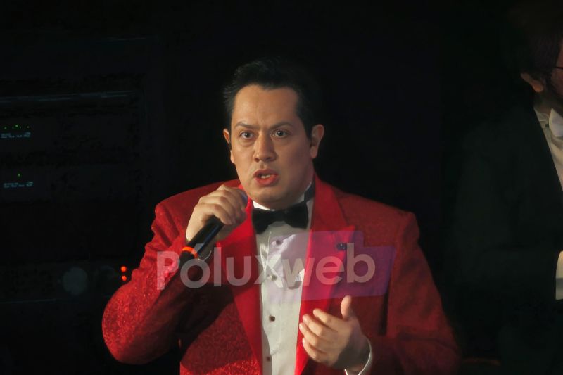 Jair Campos en Escenario El cantante Jair Campos luciendo un saco rojo y moño negro mientras interpreta una canción con gran expresividad en el micrófono.