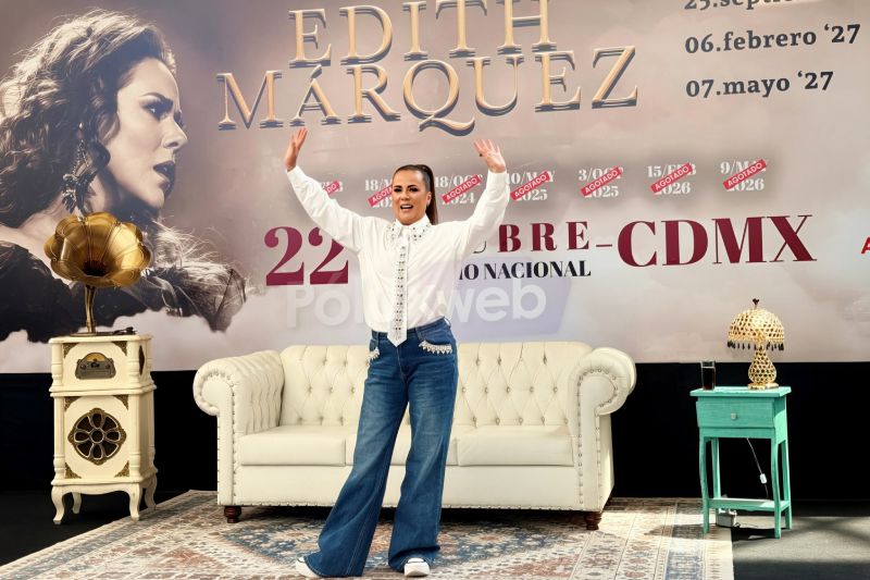 Edith Márquez anuncia su concierto en el Auditorio Nacional Edith Márquez vestida con camisa blanca decorada y jeans azulosos, posando sonriente con los brazos abiertos frente a la escenografía de su gira en la rueda de prensa.