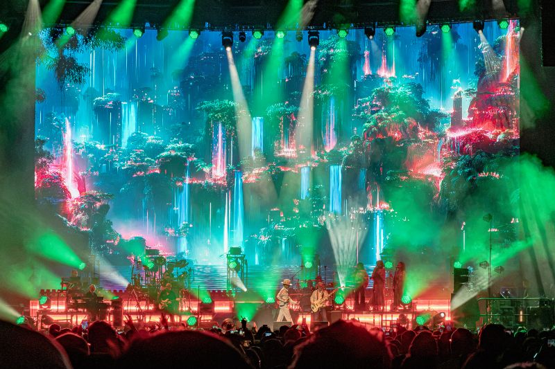 Producción visual del concierto de Jamiroquai Escenario completo de Jamiroquai con una enorme pantalla de fondo que muestra una selva futurista con cascadas y luces verdes.