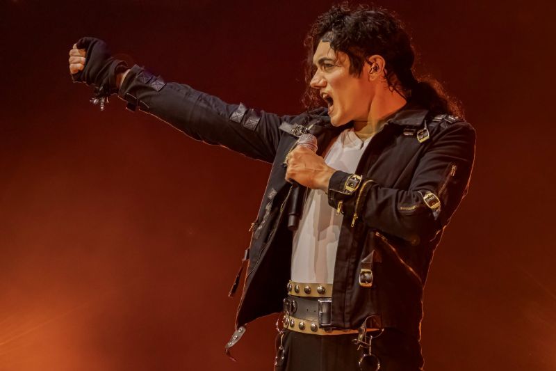 Interpretación del tema Bad El cantante con el vestuario negro táctico de la era Bad alzando el brazo con el puño cerrado ante luces rojas de fondo.
