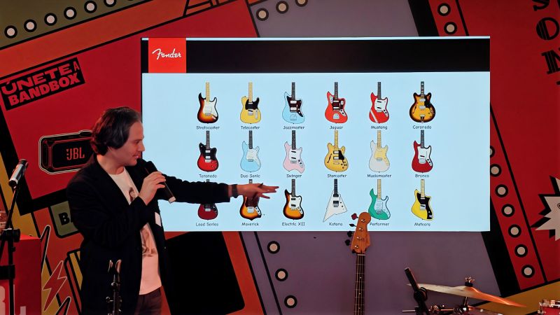 Presentación de modelos Fender en sesión informativa Presentador frente a una pantalla que muestra ilustraciones de modelos de guitarra Fender durante una sesión informativa.