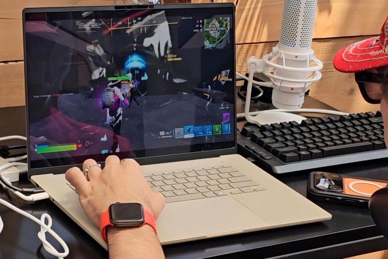 Fotografía en primer plano de un jugador utilizando una laptop impulsada por Snapdragon X durante el Bootcamp. En la pantalla se observa el videojuego Fortnite en plena partida mientras el jugador interactúa con el teclado y cuenta con un micrófono de estudio HyperX a un costado.