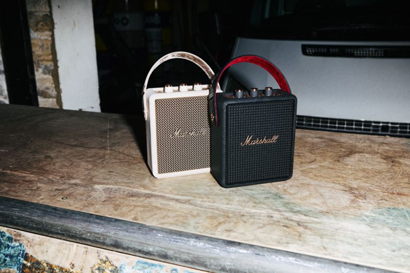 Dos altavoces portátiles Marshall, uno en color crema y otro en negro, colocados sobre una superficie de madera en un entorno industrial.