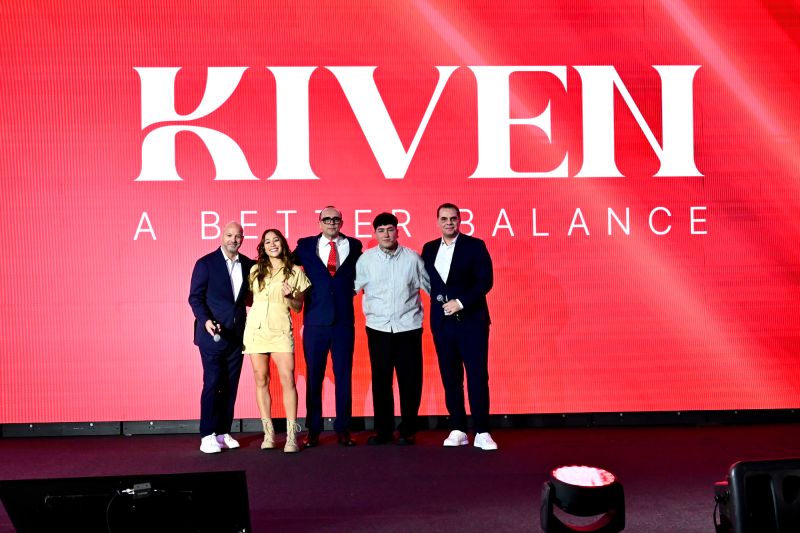 Presentación oficial de la aplicación Kiven en la Ciudad de México Directivos y presentadores parados en el escenario durante el evento de lanzamiento de Kiven en el Ex Convento de San Hipólito, con una gran pantalla roja al fondo con el logotipo de la marca.