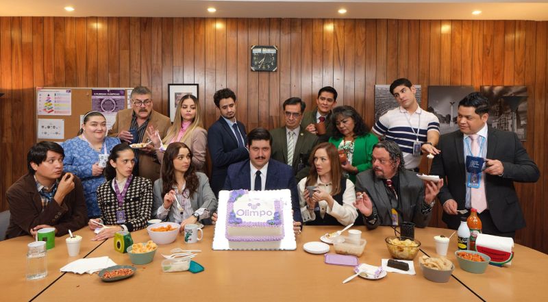 Un grupo de empleados celebra alrededor de una mesa en una oficina, con pastel, comida y ambiente festivo, evocando el tono humorístico y cotidiano de la serie.