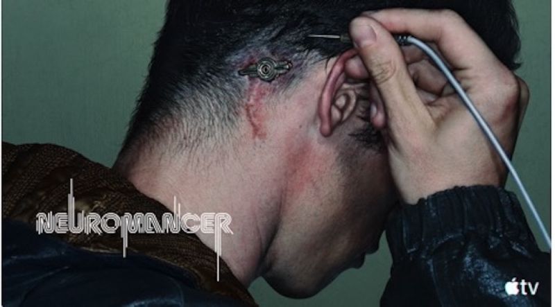 Callum Turner en primer plano con implante cibernetico en la serie Neuromante de Apple TV Fotografía de plano corto en perfil de la nuca y cabeza de un hombre con cabello oscuro corto. Detrás de su oreja se aprecia un implante cibernético metálico circular insertado en la piel con marcas de cicatriz y una pequeña incisión ensangrentada, mientras la mano sostiene una clavija conectada al puerto. En la esquina inferior izquierda aparece el logotipo oficial de "Neuromancer" y en la inferior derecha el isotipo de Apple TV.