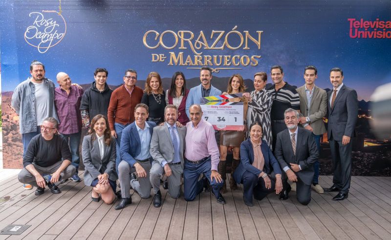 Corazón de Marruecos – Inicio de grabaciones Grupo de personas posando frente a un fondo promocional con el título de una producción televisiva, sosteniendo una claqueta durante un evento de inicio de grabaciones.
