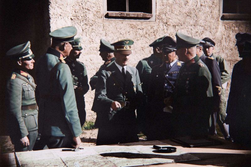 Segunda Guerra Mundial con Tom Hanks – HISTORY Grupo de oficiales militares reunidos alrededor de un mapa en un entorno exterior.