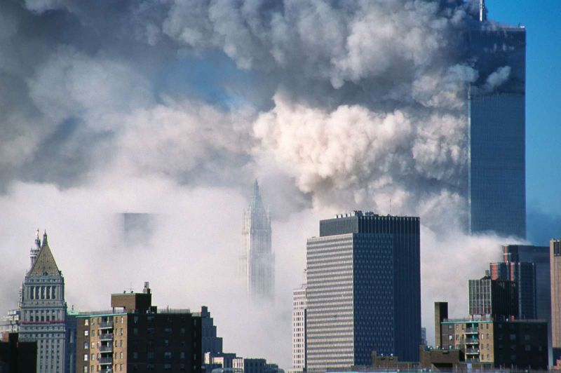 HISTORY presenta especiales documentales sobre el 11 de septiembre Vista panorámica de la zona financiera de Nueva York donde se observan densas columnas de humo blanco y gris saliendo del complejo del World Trade Center, con la silueta de una de las torres en el fondo rodeada de bruma y edificios del bajo Manhattan.