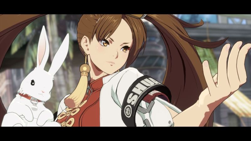 Jam Kuradoberi — Guilty Gear -Strive- Personaje femenino de estilo anime sosteniendo un conejo blanco, con vestimenta roja y detalles dorados, en un entorno urbano estilizado.