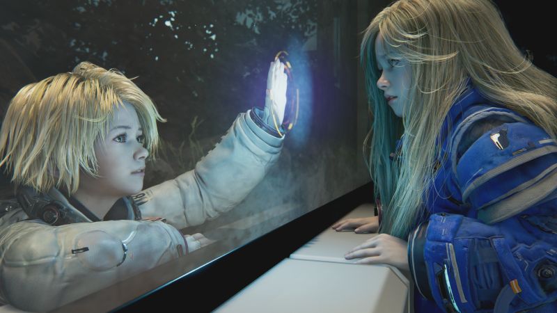 PRAGMATA – Lanzamiento global 2026 Dos personajes jóvenes separados por una superficie transparente, uno con traje futurista y otro con armadura azul, conectados por un dispositivo luminoso en un entorno oscuro.