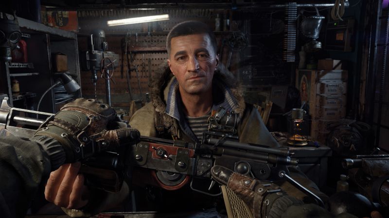 Personalización de armas y armero en METRO 2039 Captura de pantalla de jugabilidad en primera persona de METRO 2039 en resolución 4K. El jugador sostiene con ambas manos enguantadas en cuero y tela militar un arma de fuego personalizada con visor táctico y acabados metálicos. Al frente, un armero de mirada seria luciendo una chamarra de invierno con gorro de peluche y una playera marinera a rayas le entrega o examina el arma dentro de un taller repleto de herramientas, municiones y máscaras de gas de fondo.