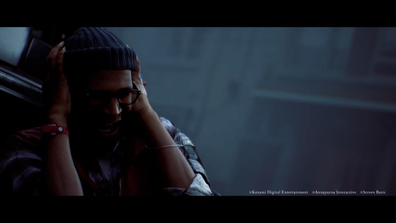 Simon Ordell sufriendo en SILENT HILL: Townfall Captura del tráiler de SILENT HILL: Townfall en resolución 4K. Un hombre de tez morena (Simon Ordell) viste un gorro azul de lana, lentes de armazón negro y una camisa a cuadros. Se encuentra gritando angustiado mientras se cubre las orejas con ambas manos con fuerza, envuelto en una atmósfera oscura, húmeda y con niebla pesada de fondo.