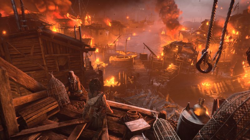 Atmósfera de poblado costero arrasado por el fuego Vista panorámica desde una plataforma elevada de un poblado portuario en llamas con barcos destruidos y fuego intenso.