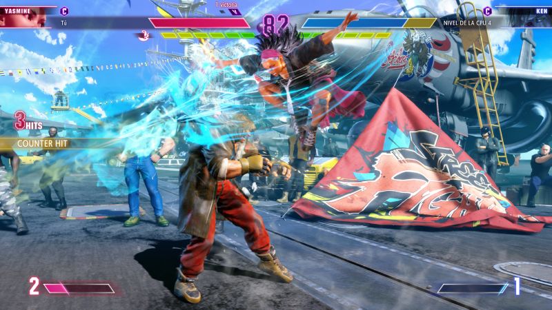 Captura de pantalla de pelea donde Yasmine salta por los aires ejecutando una patada descendente rodeada de ráfagas de viento contra Ken Masters.