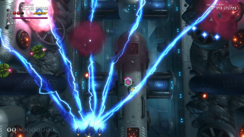 Gameplay de “Truxton Extreme” Captura de videojuego con nave espacial en combate vertical dentro de un entorno industrial.