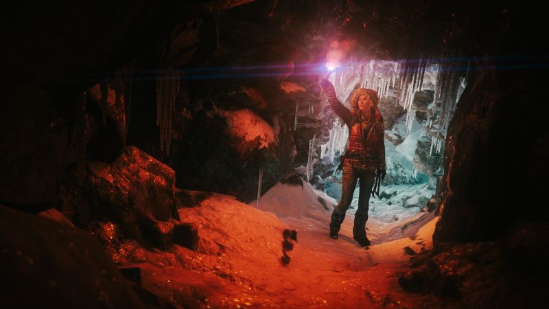 Persona sosteniendo una bengala roja dentro de una cueva helada iluminada por hielo y fuego.