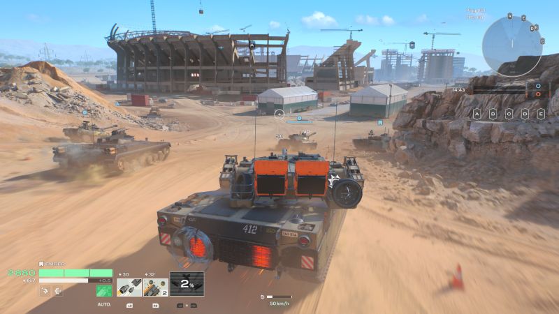 Tanque avanzando con otros vehículos hacia una estructura industrial.