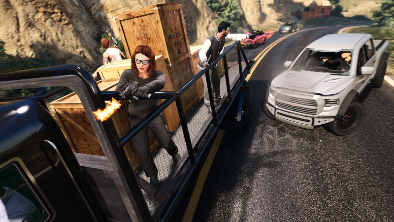 GTA Online – Actualización semanal Escena de acción con personajes armados sobre un vehículo en movimiento durante un enfrentamiento en carretera.