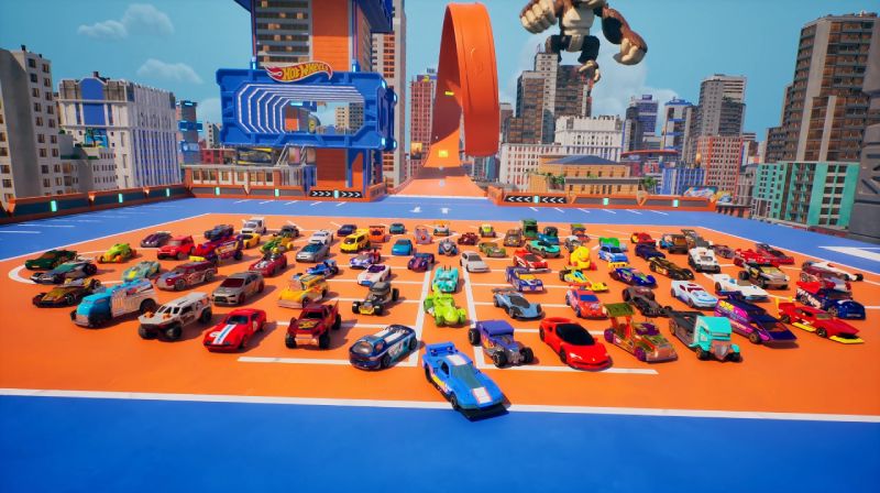 HOT WHEELS Infinite Rush ya esta disponible en consolas y PC Decenas de carritos de juguete Hot Wheels de diversos colores y estilos alineados en una plataforma azul y naranja, con rascacielos y una pista naranja gigante de fondo bajo un cielo azul.