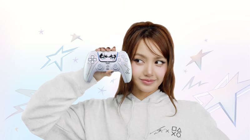 DualSense Edicion Limitada LISA PlayStation 5 La cantante e ícono de K-Pop LISA sosteniendo el nuevo control inalámbrico DualSense Edición Limitada frente a su rostro. El control presenta un diseño blanco perlescente Chroma Pearl con ilustraciones negras en el touchpad de sus ojos y flequillo, y letras LL en las empuñaduras, rodeada de ilustraciones de estrellas brillantes.