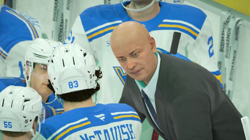 Primer plano de un entrenador calvo en traje dando instrucciones a sus jugadores con casco de hockey sobre hielo en la banca.
